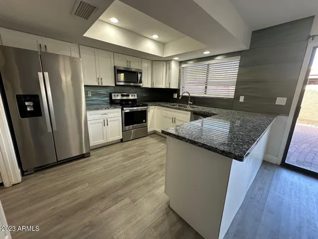 a kitchen with granite countertop a refrigerator a sink dishwasher a stove and white countertops with wooden floor