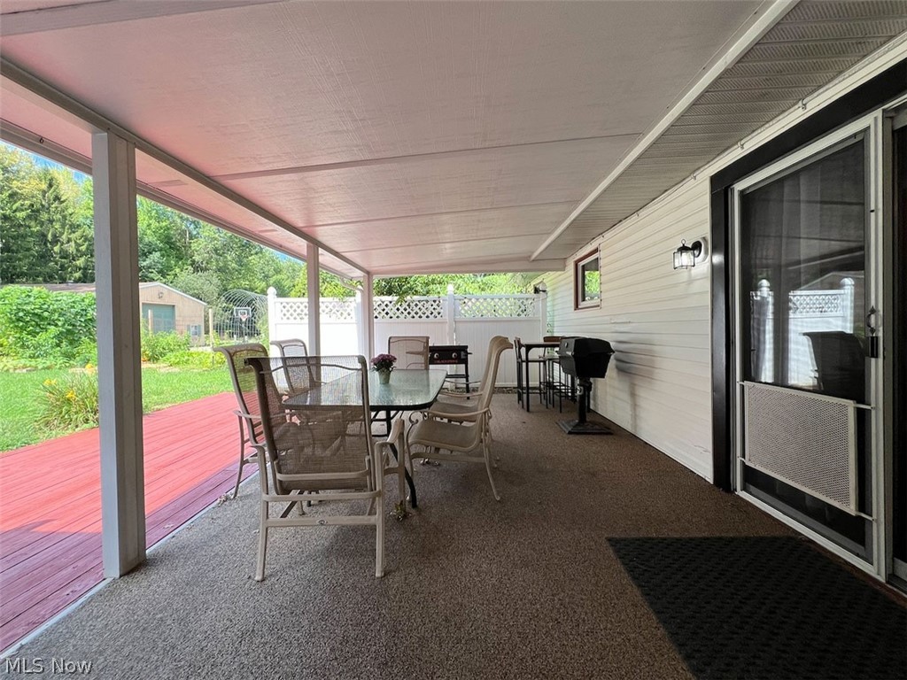 5841 Horning Road Kent, OH 44240 - Photo 20 of 31 Covered patio with textured flooring, a red wood-finish deck extension, white vinyl siding, and exterior lighting