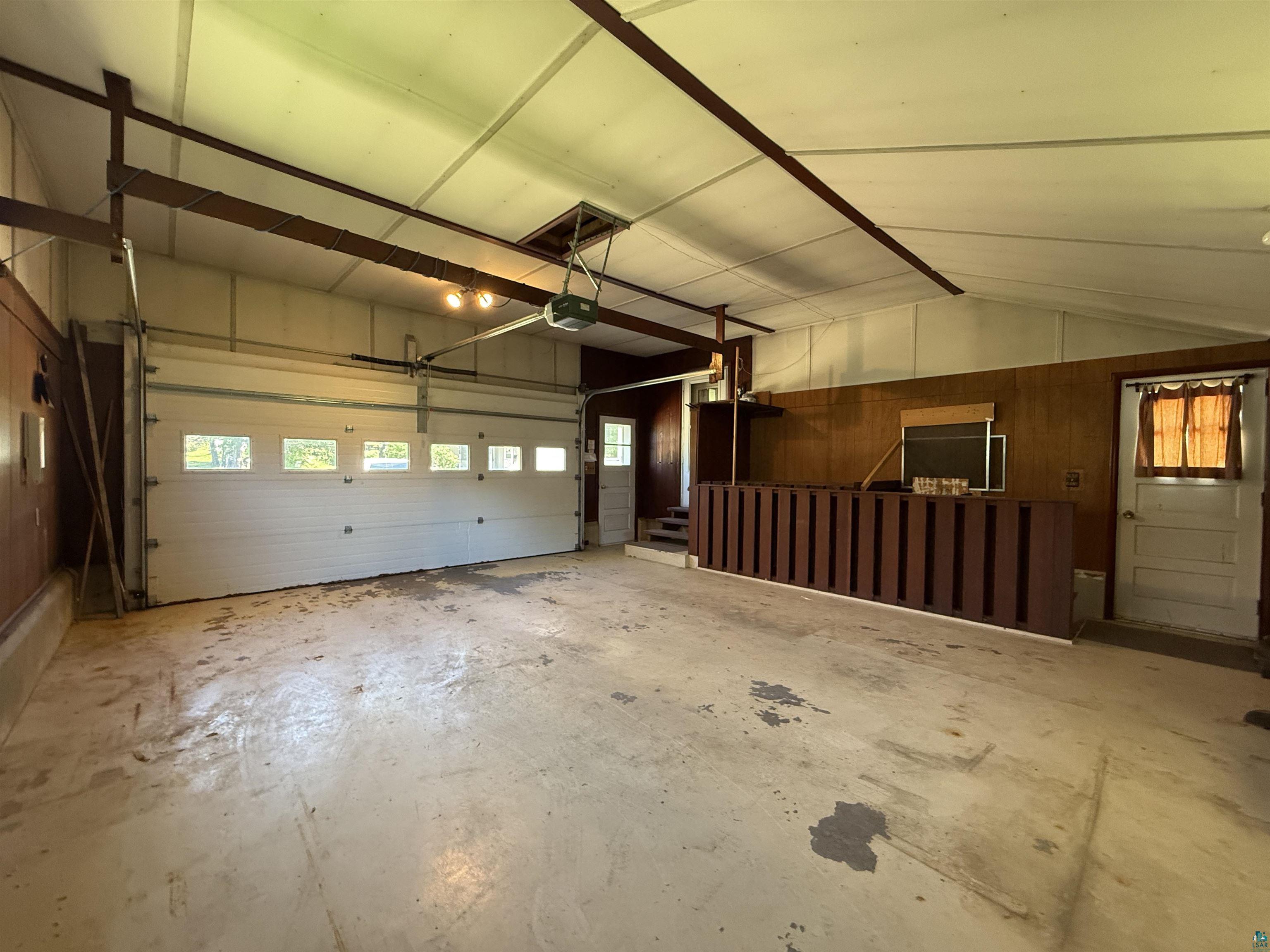 607 3rd Street Northeast Chisholm, MN 55719 - Photo 28 of 32 Garage featuring a sectional overhead door with transom windows, exposed ceiling joists, wood-paneled walls, and a separate service door