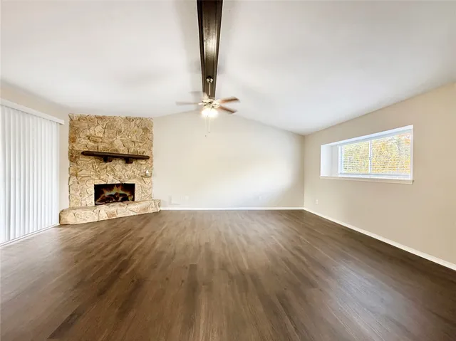 an empty room with wooden floor fireplace and windows