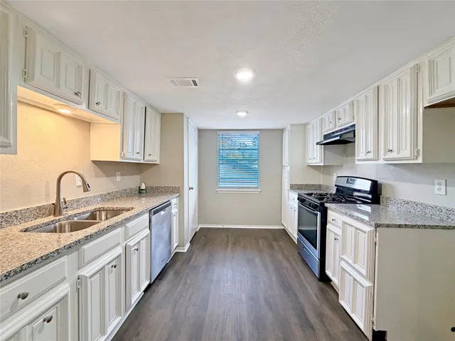 a kitchen with granite countertop a sink cabinets stainless steel appliances and a window