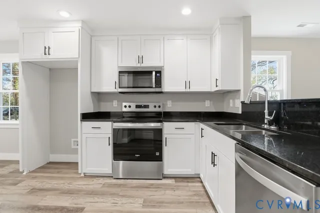 a kitchen with granite countertop white cabinets a sink and appliances