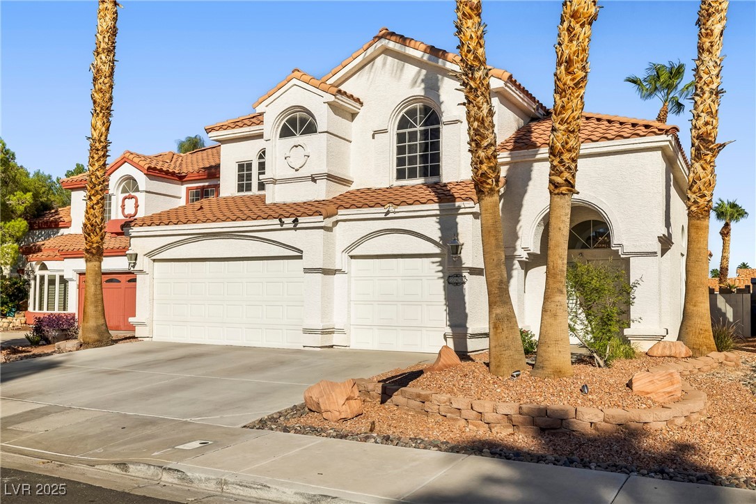 Mediterranean / spanish-style house with a tiled roof, driveway, and stucco siding