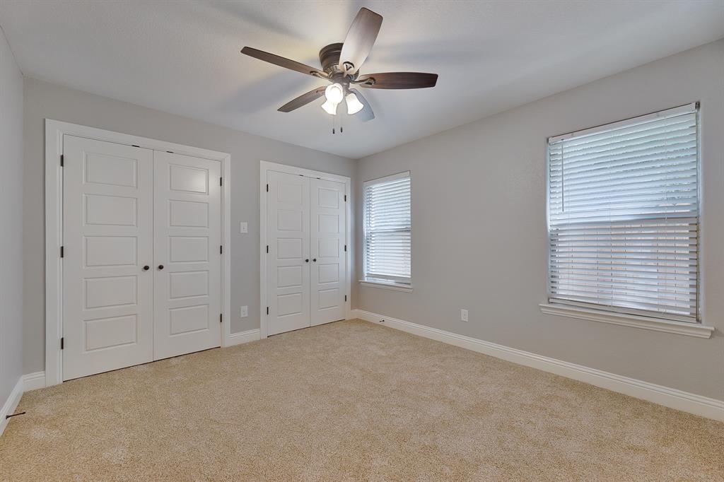 1713 Bronco Road Granbury, TX 76049 - Photo 12 of 23 Carpeted room featuring two sets of paneled double-door closets, two windows with blinds, a ceiling fan with integrated lighting, and neutral wall paint