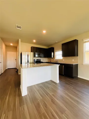 a large kitchen with stainless steel appliances kitchen island a large counter top a stove and a wooden floor