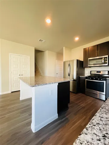 a kitchen with stainless steel appliances kitchen island granite countertop a stove a refrigerator and a sink with wooden floor