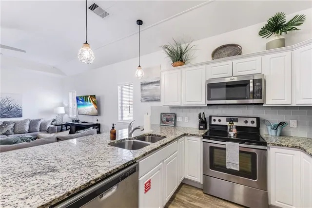 a kitchen with stainless steel appliances granite countertop a sink a stove a microwave a refrigerator and white cabinets