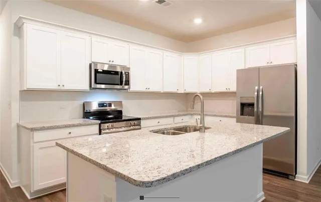 a kitchen with stainless steel appliances granite countertop a sink a microwave a refrigerator and white cabinets