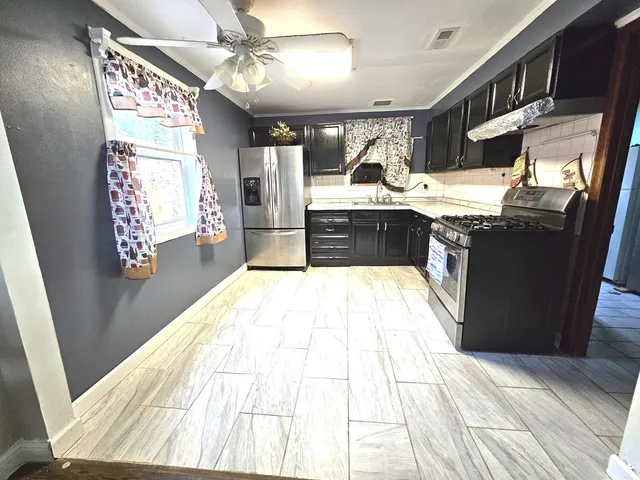 a kitchen with stainless steel appliances kitchen island granite countertop a refrigerator a stove and a wooden floors