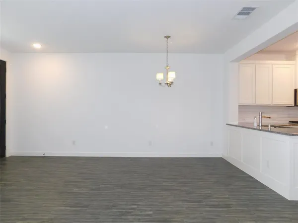 a view of an empty room with wooden floor and kitchen space
