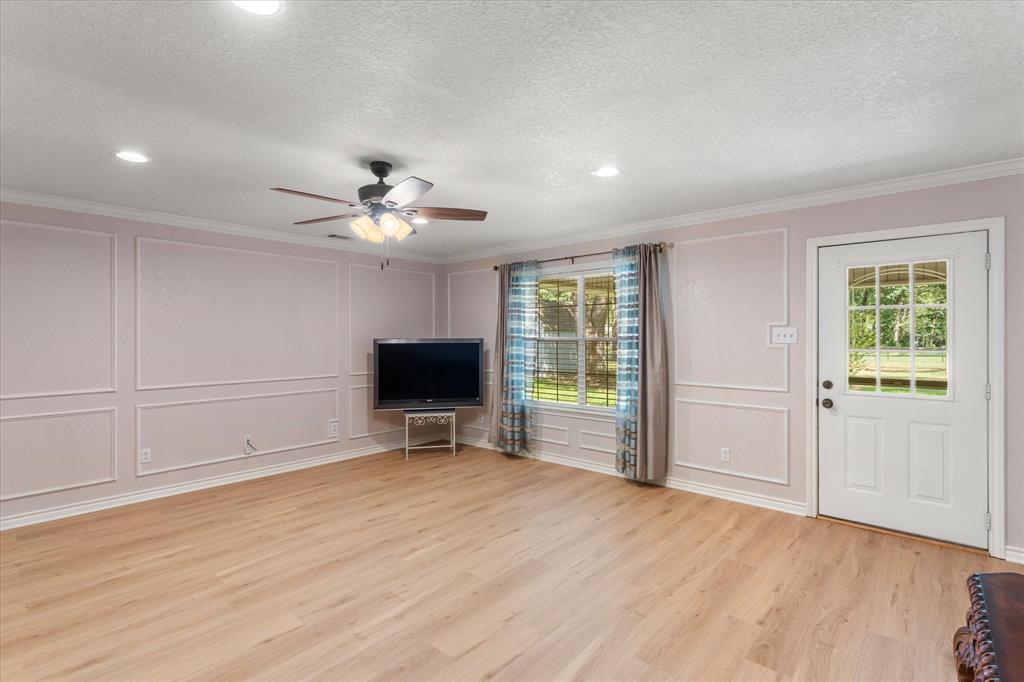 116 Meadowood Road Enchanted Oaks, TX 75156 - Photo 19 of 37 Spacious room featuring light wood-finish flooring, decorative wall molding, a ceiling fan with integrated lighting, recessed ceiling lights, and a white paneled door with a multi-pane glass insert