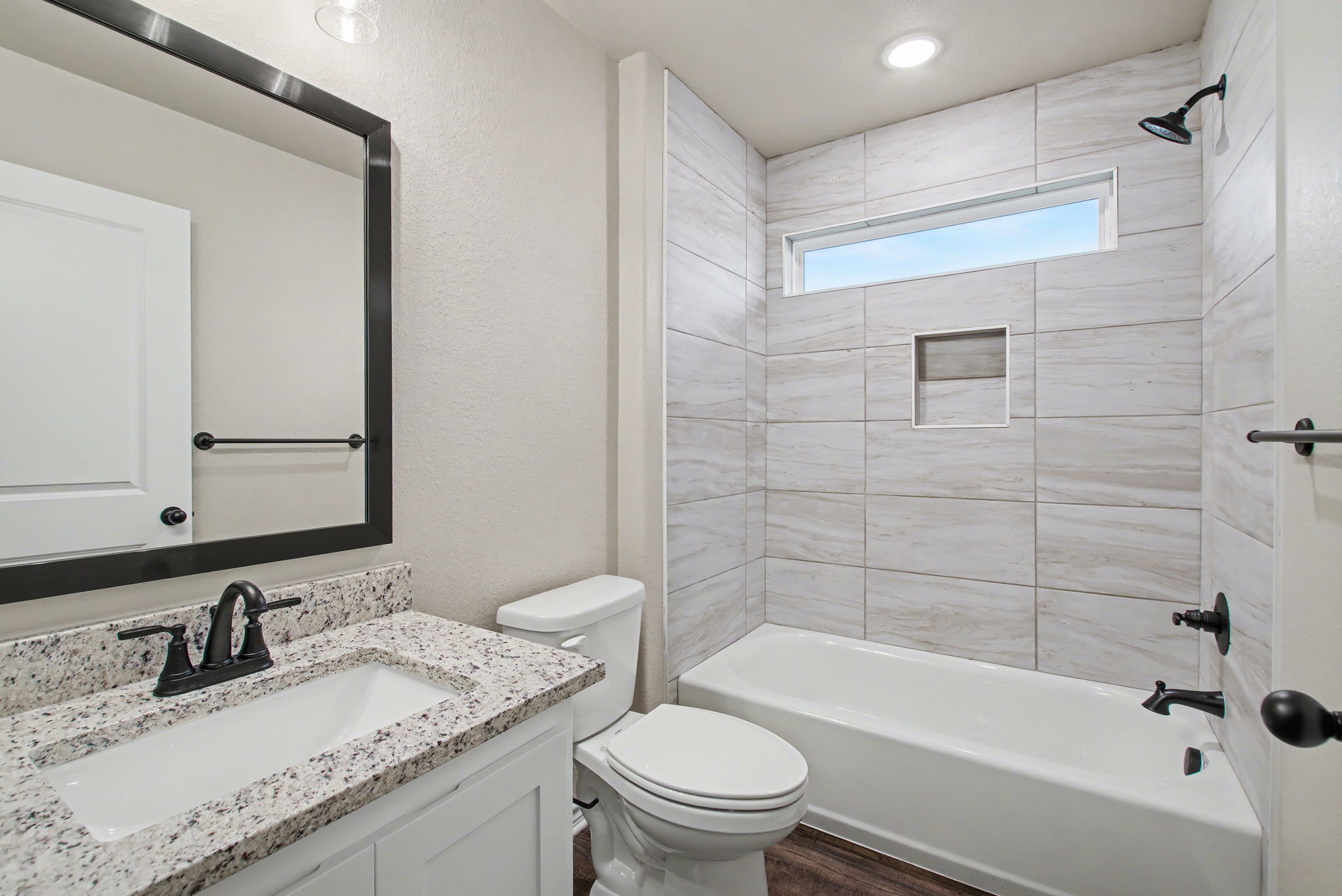 206 Water Wl Road Burnet, TX 78611 - Photo 17 of 25 A modern bathroom features a tiled shower surround, stone-topped vanity, and a transom window.