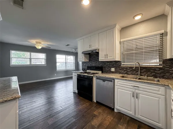 a kitchen with stainless steel appliances granite countertop wooden cabinets a sink a stove a microwave and wooden floors