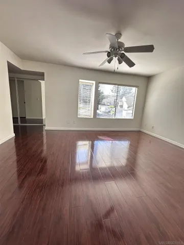 an empty room with wooden floor chandelier fan and windows