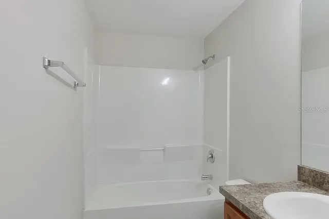a bathroom with a granite countertop bathtub shower sink vanity and toilet