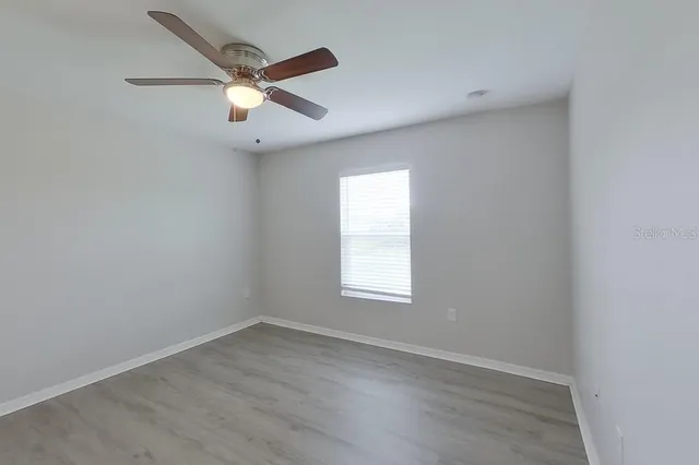 an empty room with wooden floor ceiling fan and windows