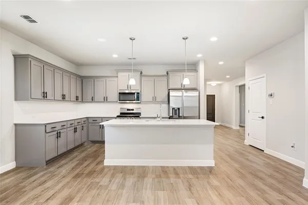 a large kitchen with stainless steel appliances granite countertop a large center island a stove a refrigerator cabinets and a wooden floor