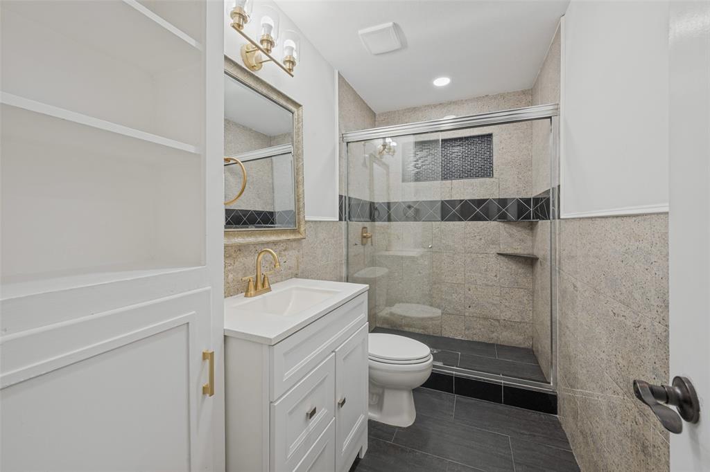 3584 Regal Road Fort Worth, TX 76111 - Photo 8 of 12 Built-in shelving, vanity with white shaker-style cabinetry, gold-finish faucet, and a glass-enclosed shower with tiled walls