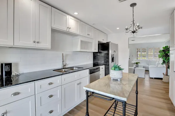 a kitchen with granite countertop white cabinets a sink dishwasher and a stove with wooden floor