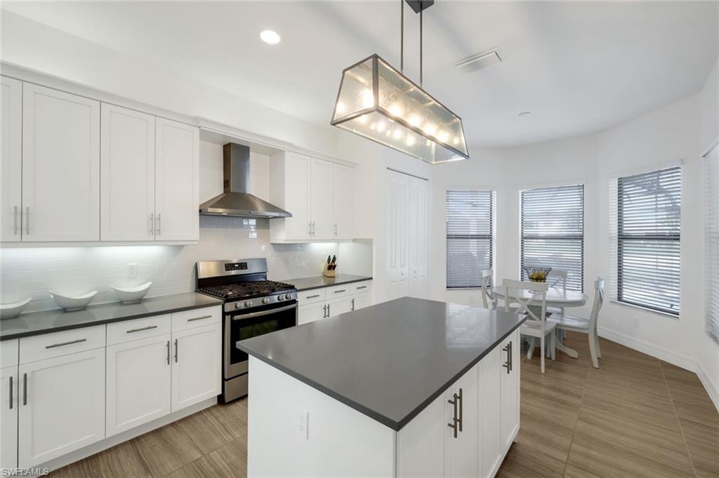4549 Azalea Drive Naples, FL 34119 - Photo 15 of 49 a kitchen with stainless steel appliances granite countertop a sink dishwasher a stove a dining table and chairs with wooden floor