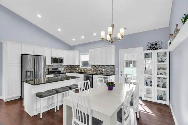 a kitchen with stainless steel appliances granite countertop a refrigerator a stove top oven a sink dishwasher a dining table and chairs with wooden floor