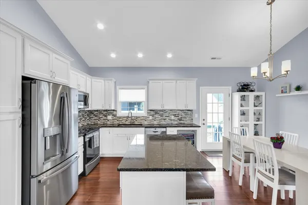 a kitchen with stainless steel appliances granite countertop a refrigerator a stove a sink dishwasher a refrigerator and white cabinets with wooden floor