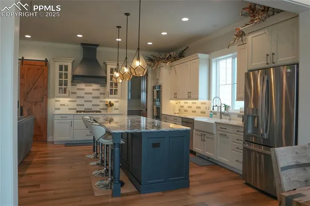 a kitchen with stainless steel appliances kitchen island granite countertop a refrigerator a stove and a wooden floors