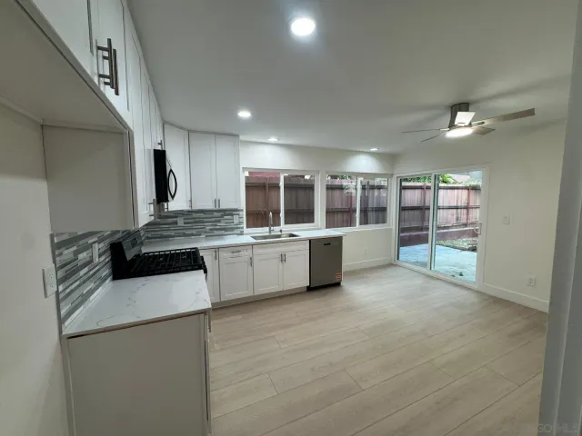 a large white kitchen with a sink and dishwasher a stove top oven with wooden floor