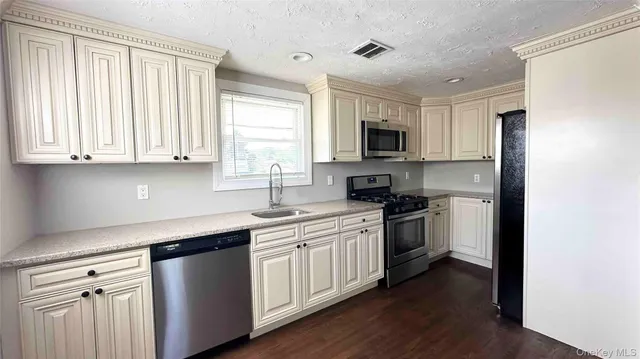 a kitchen with stainless steel appliances granite countertop white cabinets a sink and a window