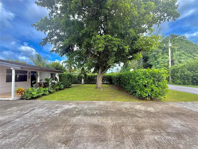 a view of yellow house with a big yard and large trees