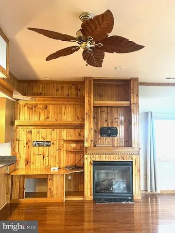 a view of an empty room with wooden floor a ceiling fan and windows