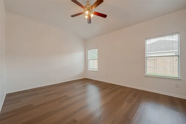 an empty room with wooden floor ceiling fan and windows