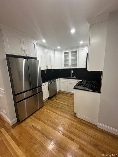 Kitchen featuring dark countertops, appliances with stainless steel finishes, white cabinets, light wood-type flooring, and glass insert cabinets