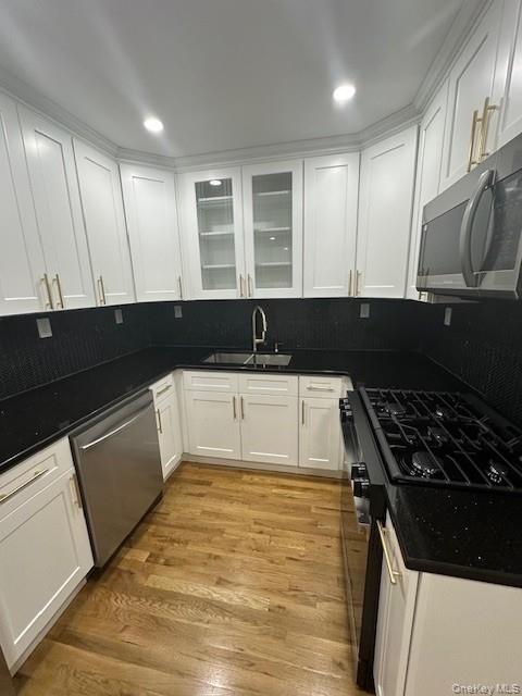 3524 Cambridge Avenue, Unit C Bronx, NY 10463 - Photo 2 of 10 Kitchen featuring stainless steel appliances, white cabinetry, decorative backsplash, glass insert cabinets, and light wood-type flooring