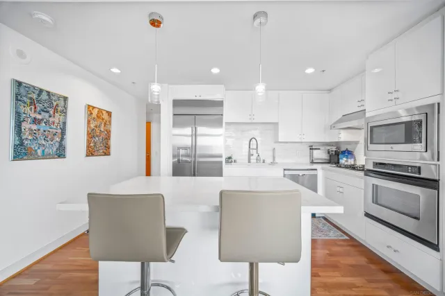 a kitchen with stainless steel appliances granite countertop a refrigerator a stove a sink a dining table and chairs with wooden floor