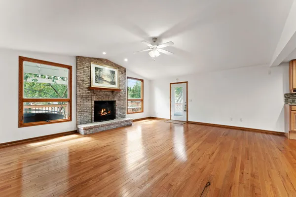 a view of an empty room with wooden floor fireplace and a window