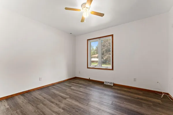 an empty room with wooden floor ceiling fan and windows