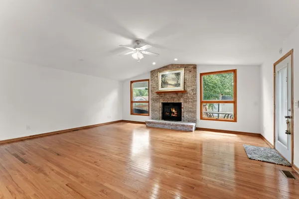 an empty room with wooden floor fireplace and windows