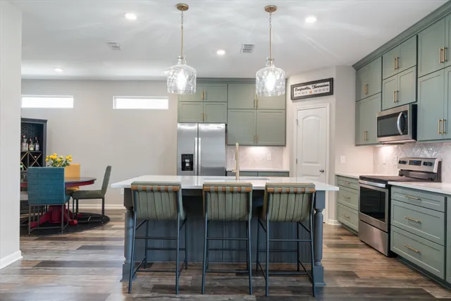 a kitchen with stainless steel appliances granite countertop a stove a refrigerator a kitchen island a dining table and chairs with wooden floor