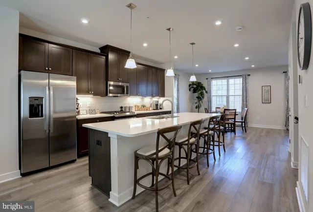a kitchen with stainless steel appliances kitchen island granite countertop a refrigerator a stove a sink a dining table and chairs with wooden floor