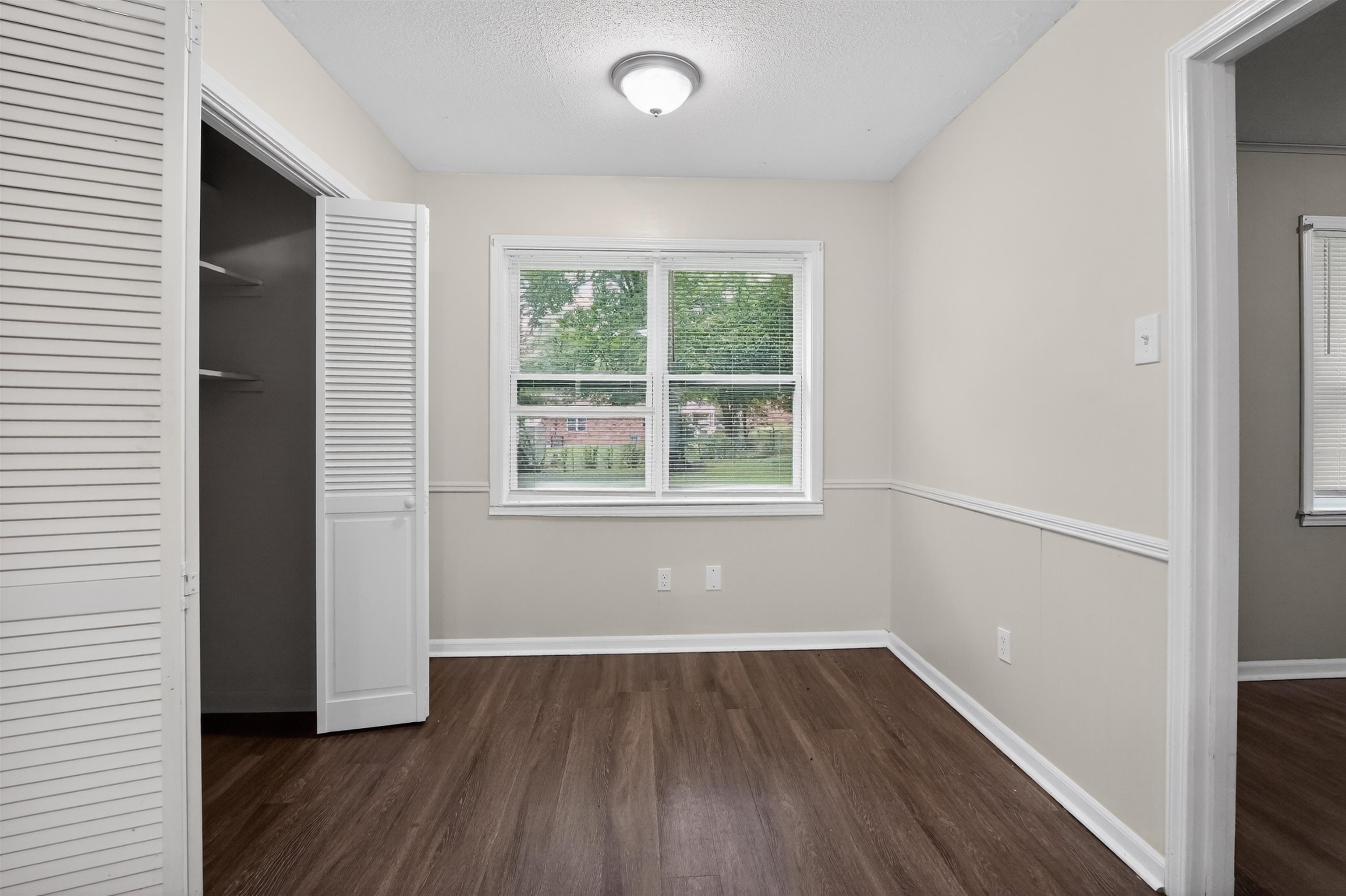 3152 Mackham Avenue Memphis, TN 38118 - Photo 13 of 16 Room featuring wood-finish flooring, a window with exterior visibility, a built-in closet with louvered bi-fold doors, and a ceiling-mounted light fixture
