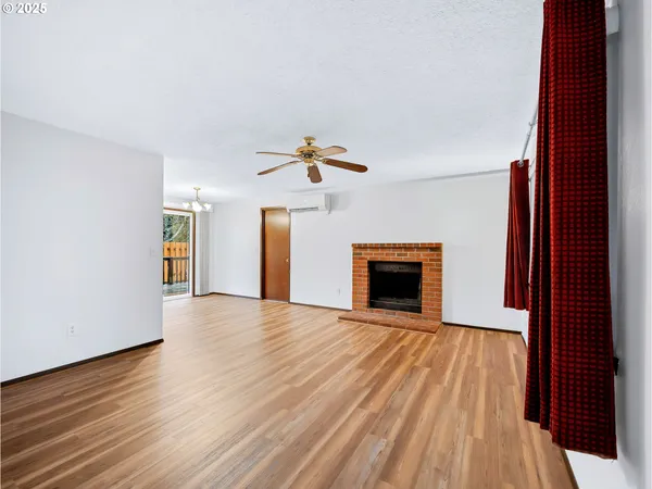a view of an empty room with wooden floor fireplace and a window