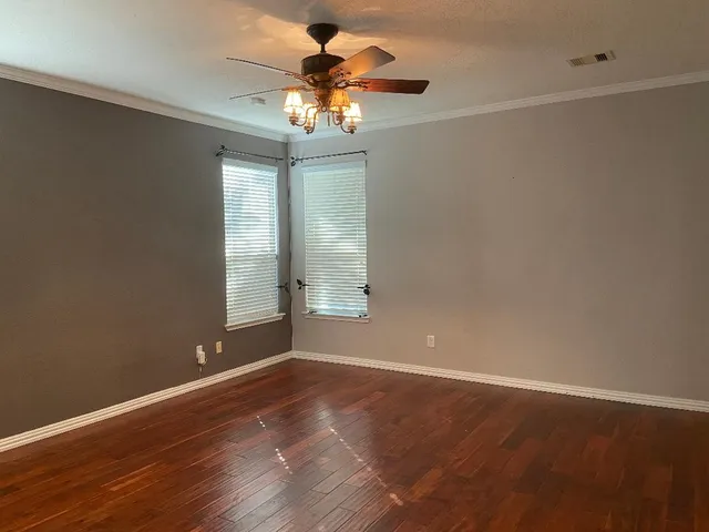 an empty room with wooden floor chandelier fan and windows