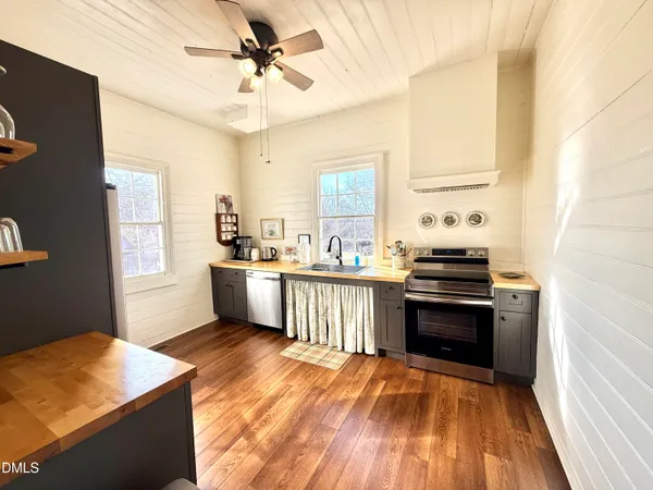 a kitchen with stainless steel appliances granite countertop a refrigerator a sink dishwasher a stove and white countertops with wooden floor