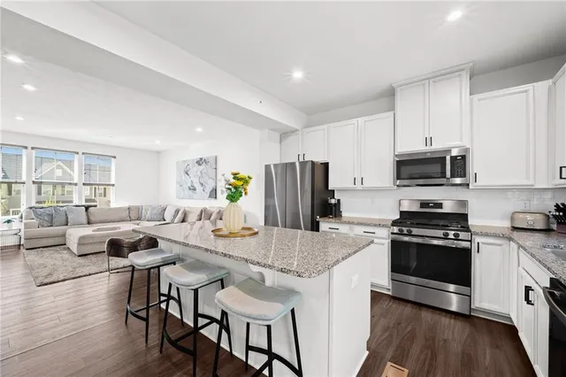 a kitchen with stainless steel appliances granite countertop a stove a sink dishwasher a microwave oven a refrigerator with white cabinets and wooden floor