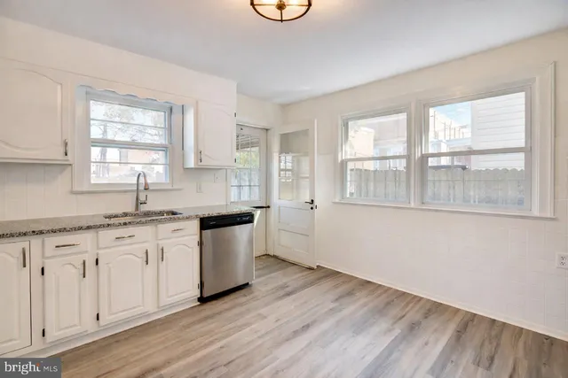 a kitchen with granite countertop a stove a sink and white cabinets with wooden floor next to windows