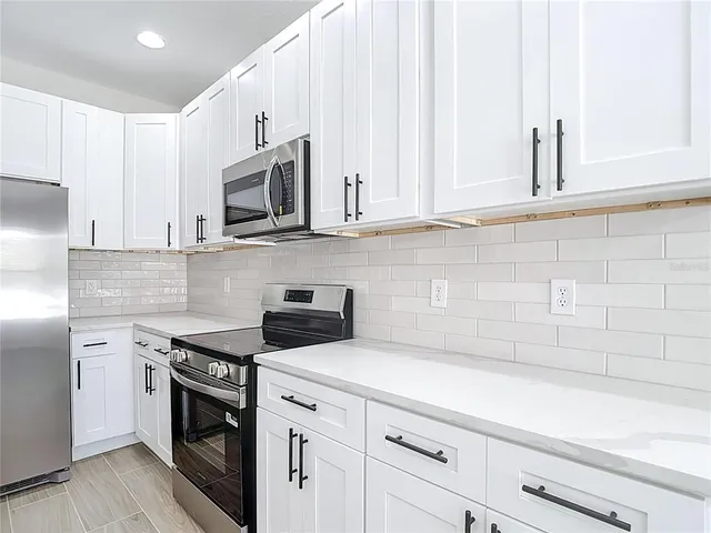 a large white kitchen with kitchen island a sink dishwasher a refrigerator and white cabinets with wooden floor