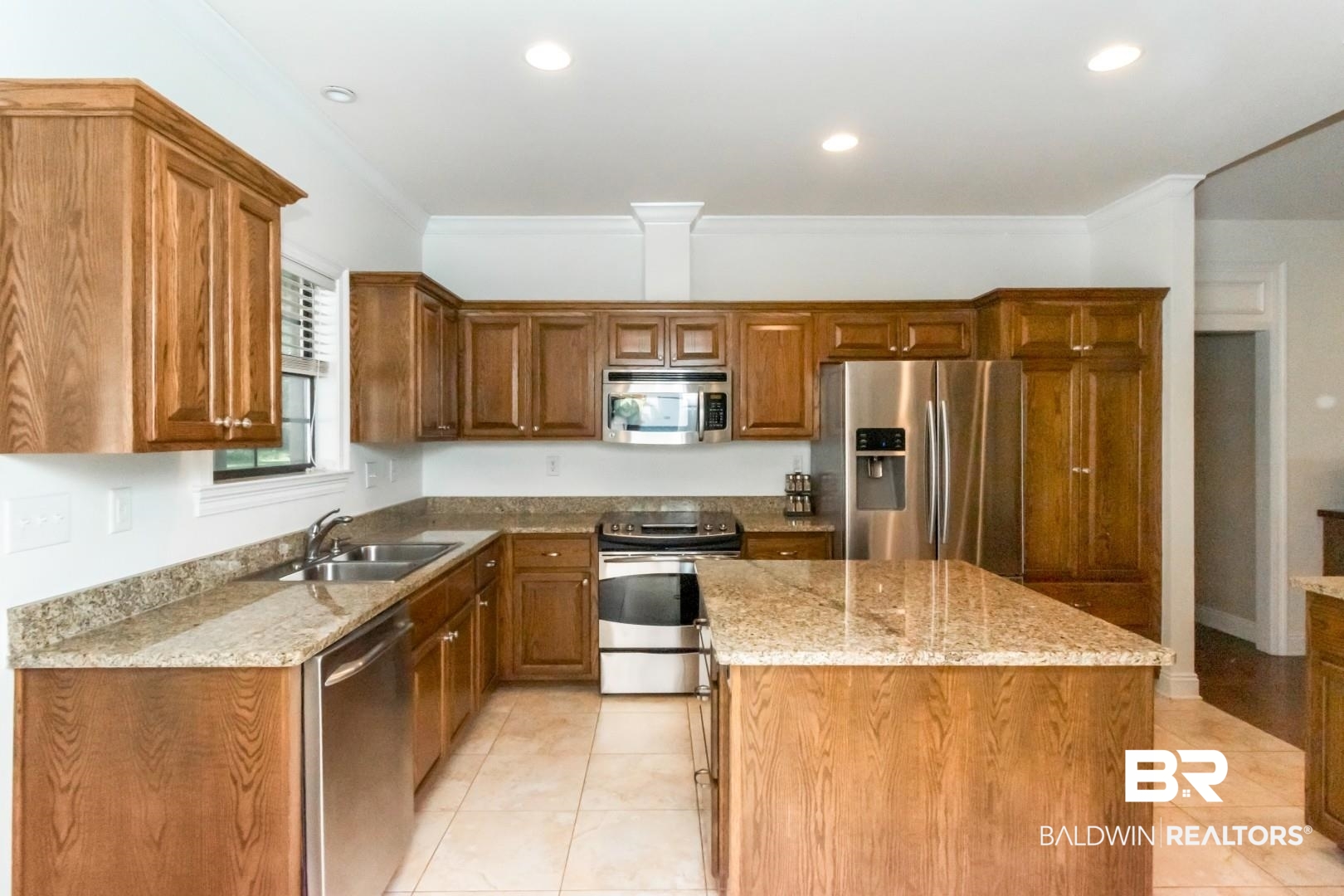 1360 Dykes Road North Mobile, AL 36608 - Photo 12 of 40 Kitchen with appliances with stainless steel finishes, light tile patterned flooring, brown cabinetry, a kitchen island, and ornamental molding