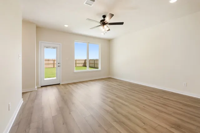 an empty room with wooden floor chandelier fan and windows