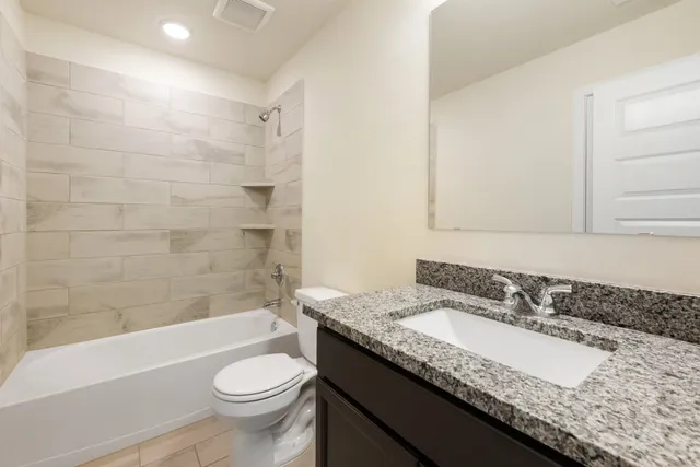 a bathroom with a granite countertop sink a toilet a mirror and bathtub
